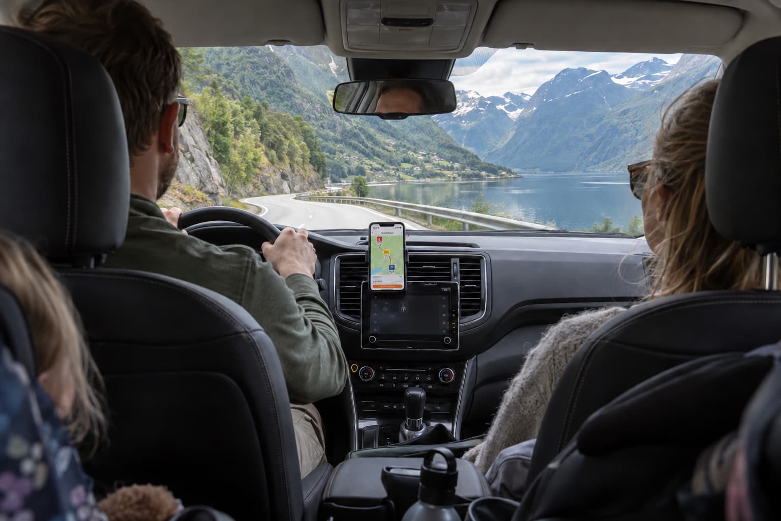 Familie på biltur langs en fjord, med DrivstoffAppens ruteplanlegger på mobilen i dashbordholderen